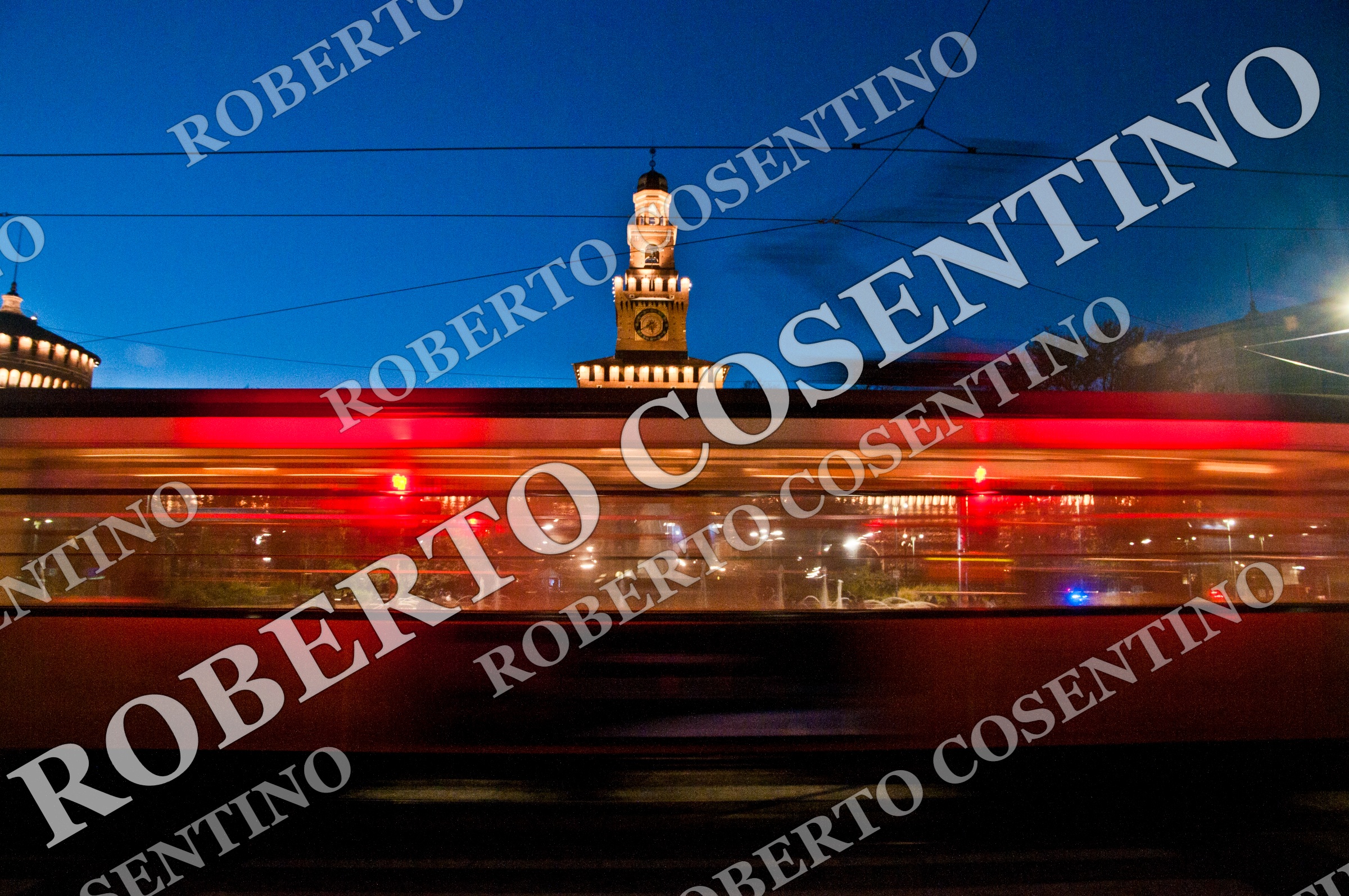 Tram rosso in movimento davanti alla Torre del Filarete del Castello Sforzesco, a Milano, al crepuscolo.